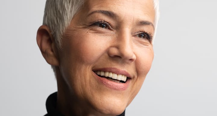 Maquillage naturel sur peau mature ; gros plan d’un modèle souriant aux cheveux gris courts et au teint uniforme