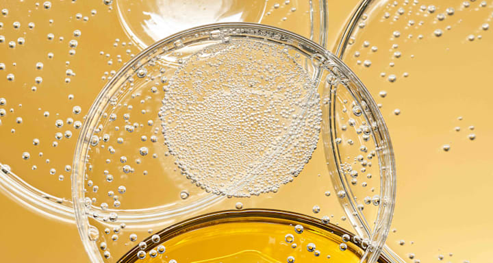 Gelartige Textur mit vielen kleinen Luftblasen in transparenter Flüssigkeit auf goldenem Hintergrund, Makroaufnahme einer Serumstruktur