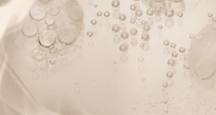 Texture gel transparente avec nombreuses bulles d’air de tailles variées dans un liquide laiteux, macro d’une texture cosmétique