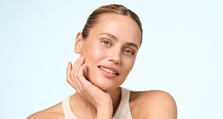 Beauty-Porträt einer lächelnden Frau mit natürlichem Make-up und einer Hand an der Wange