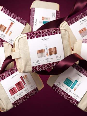 Produktbild mehrerer M. Asam Kosmetik-Geschenksets in beigen Taschen mit bordeauxroten Schleifen