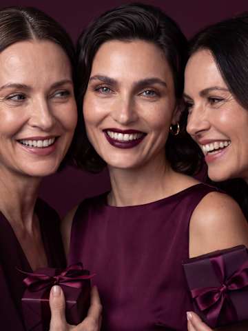 Beauty-Porträt von drei lächelnden Frauen mit Make-up und bordeauxroten Geschenkboxen