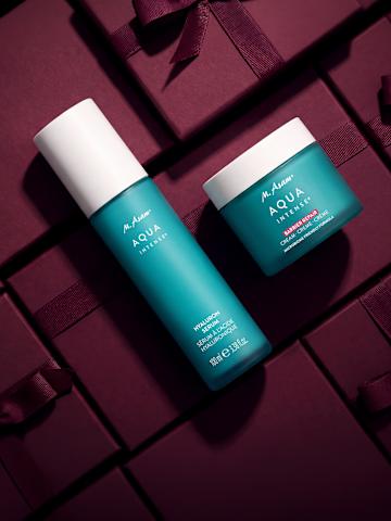 Produktbild von zwei M. Asam AQUA INTENSE Pflegeprodukten auf bordeauxroten Geschenkboxen