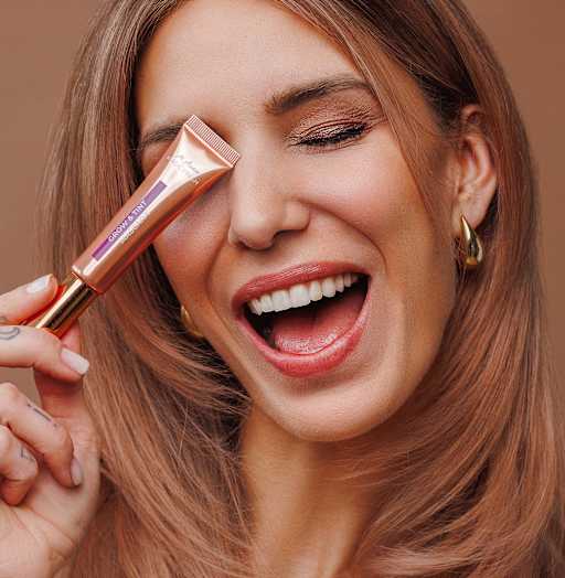 Beauty-Porträt Frau mit Mascara-Tube am Auge, Make-up in warmen Tönen
