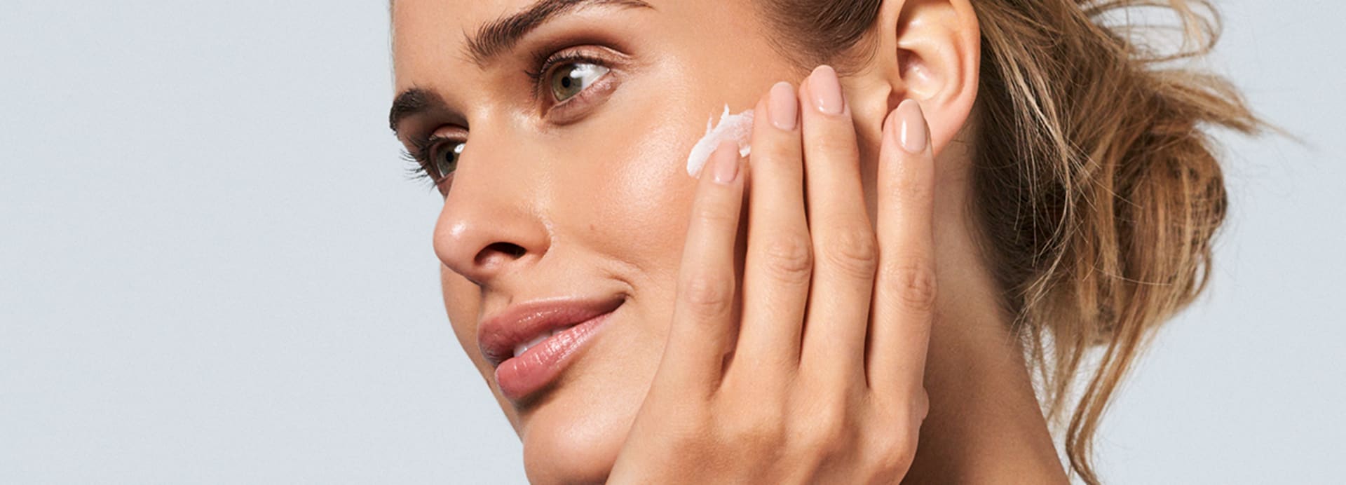Frau trägt Sonnencreme von M. Asam mit den Fingern auf die Wange auf