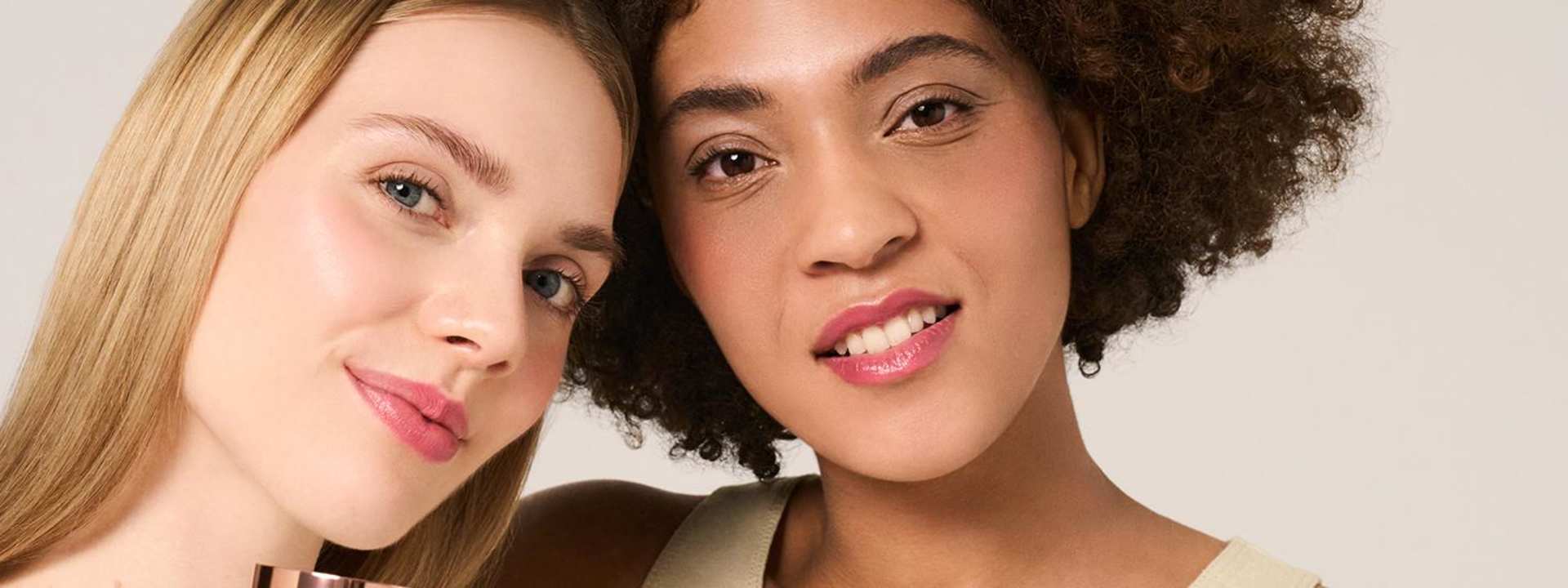 Zwei junge Frauen mit unterschiedlichen Haut- und Haartypen lächeln und halten das M. Asam MAGIC FINISH Make-up Mousse in die Kamera.