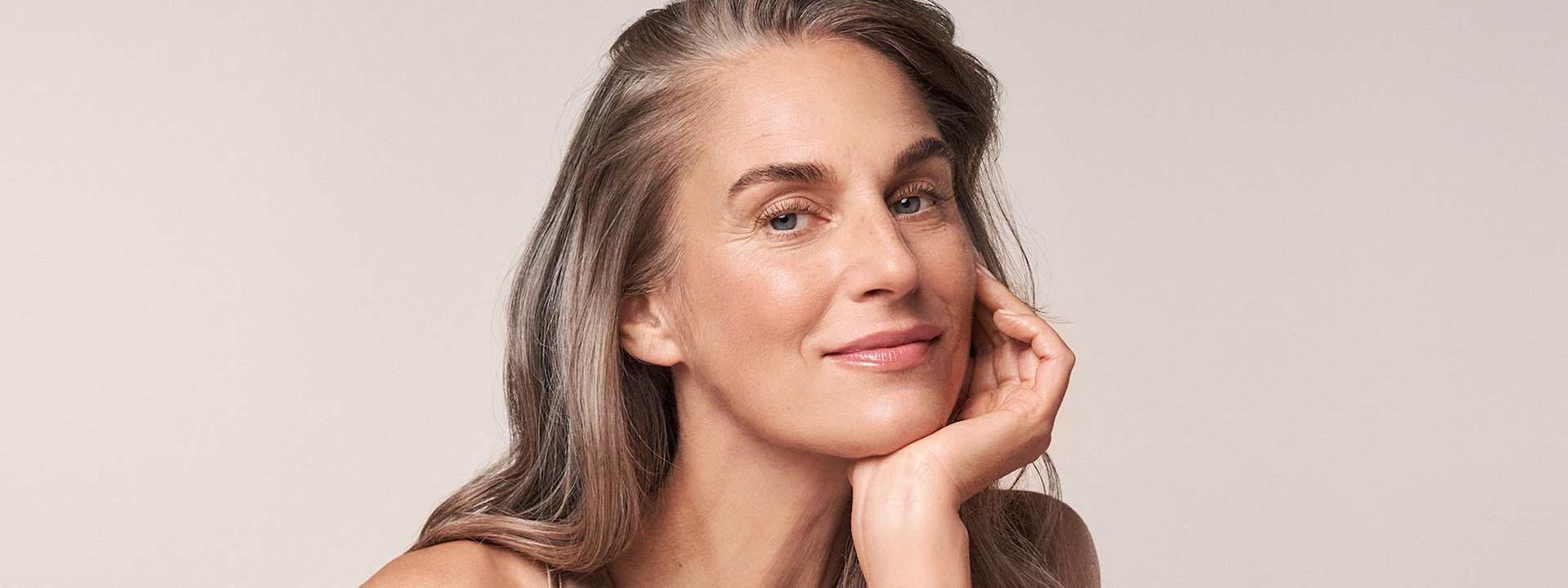 Une femme regarde l’objectif avec un air détendu après avoir appliqué les soins raffermissants RESVERATROL PREMIUM NT50.