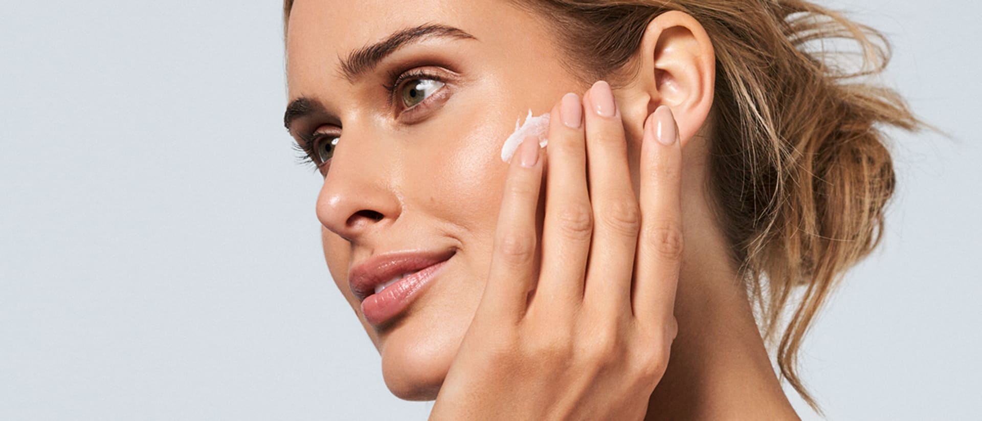 Frau trägt Sonnencreme von M. Asam mit den Fingern auf die Wange auf