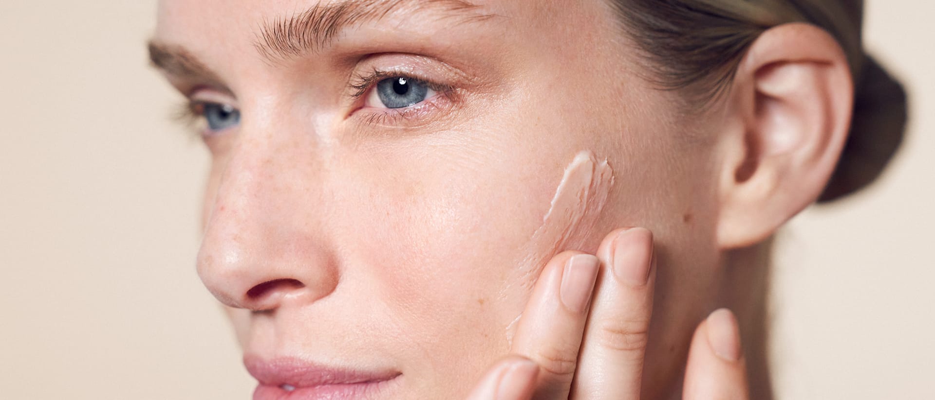 Frau trägt einen Primer von M.Asam mit den Fingern auf die Wange auf