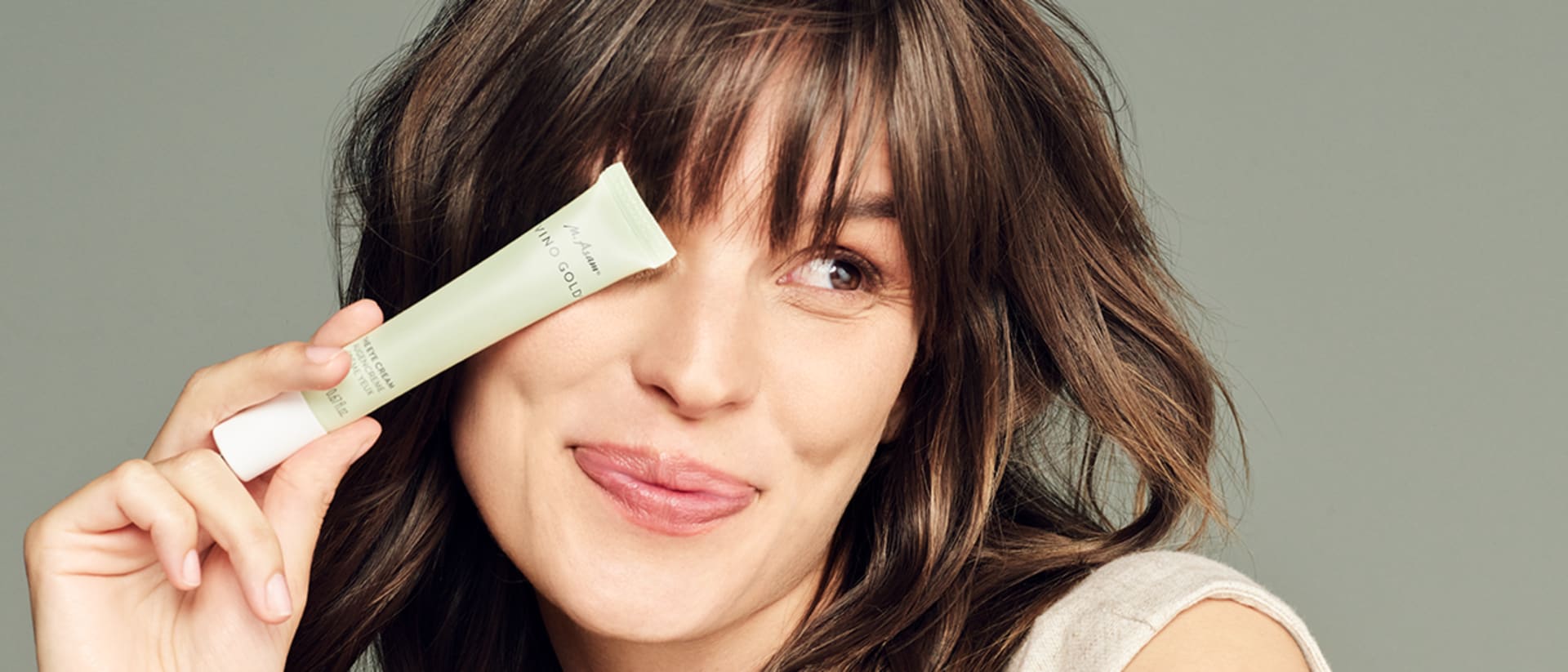 Frau hält die M. Asam VINO GOLD Augencreme vor ihr rechtes Auge und lächelt.