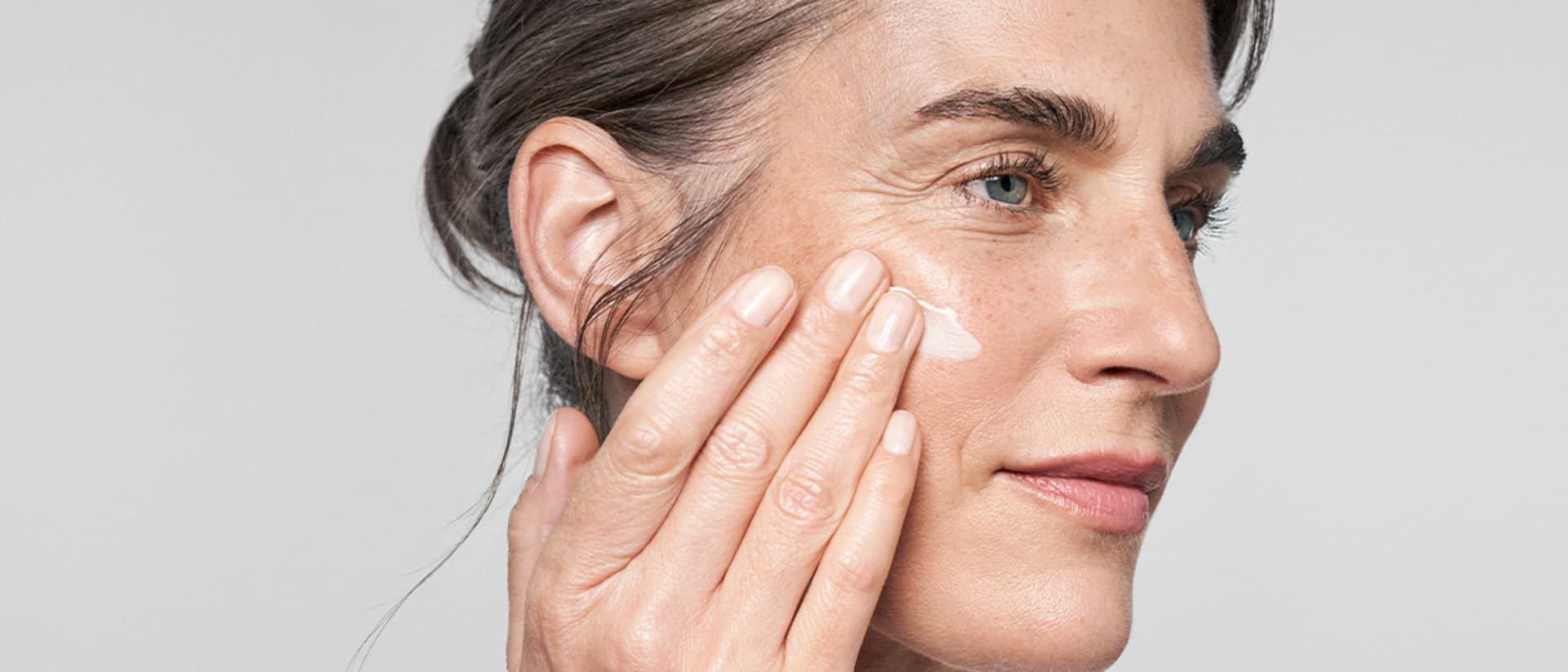 Une femme applique la crème lifting RESVERATROL PREMIUM NT50 de M. Asam sur sa joue – vue de côté.