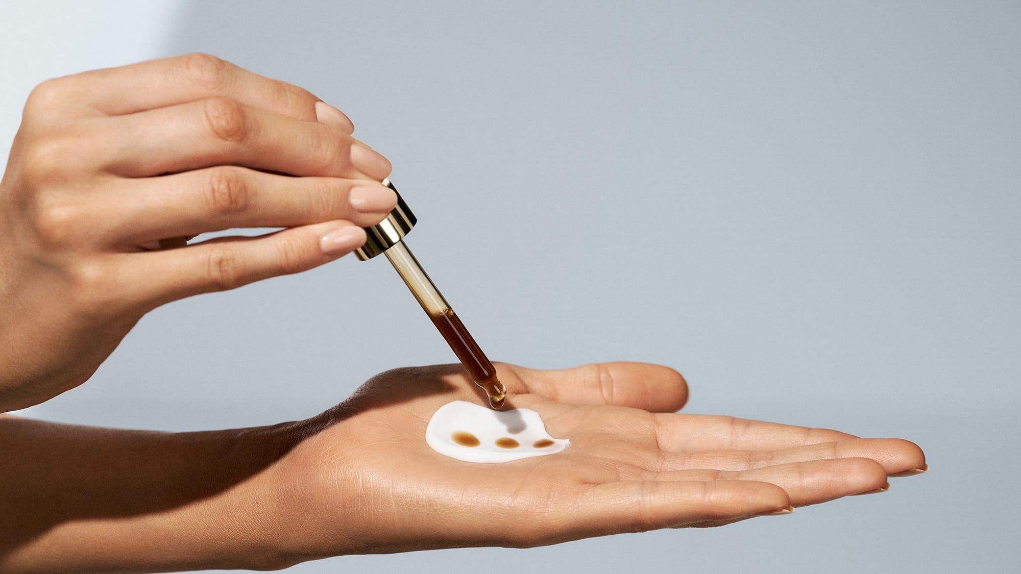 Frau mischt die Sun Self Tanning Drops von M. Asam in ihre Gesichtscreme.