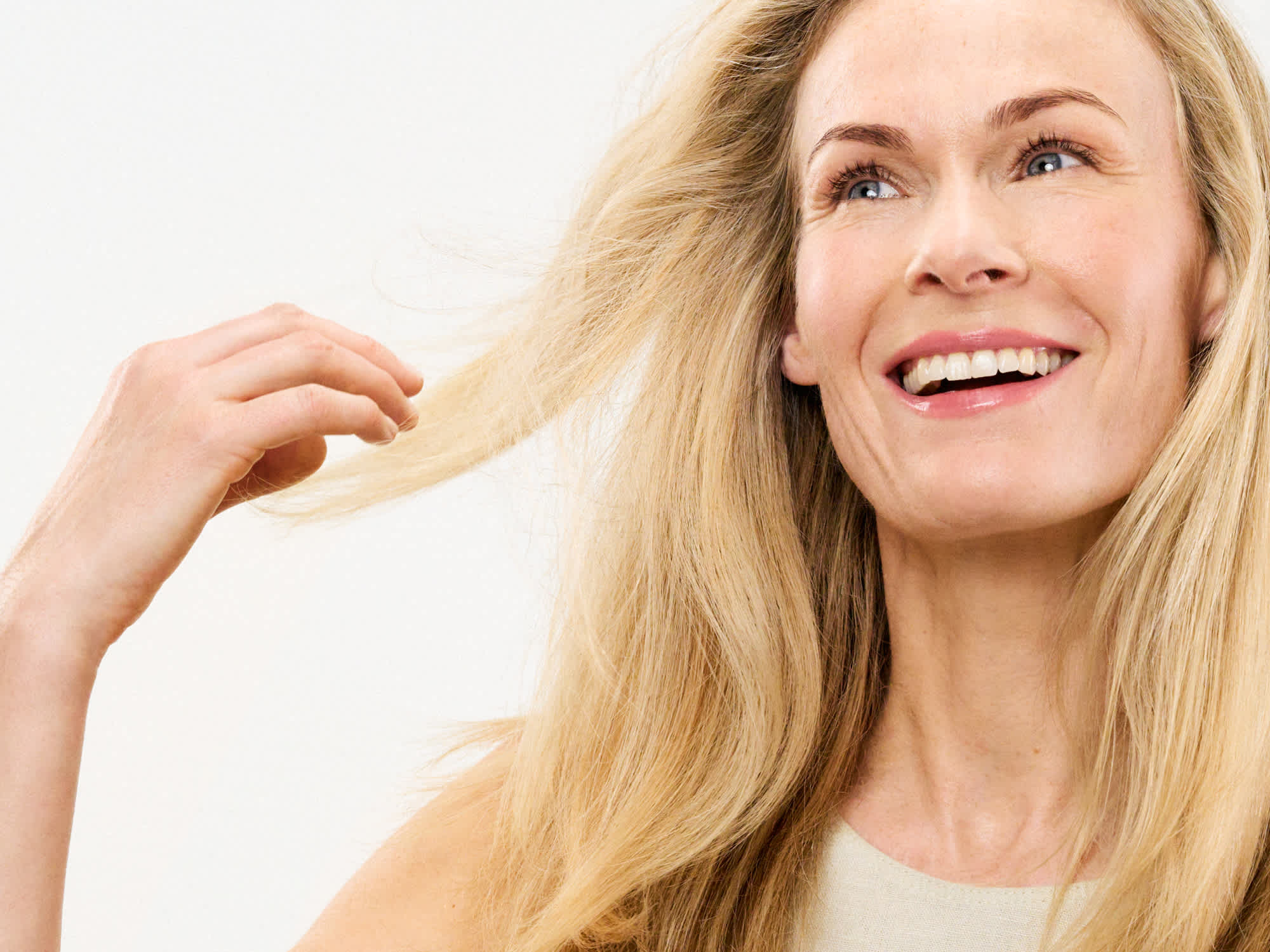 Beauty-Porträt einer lächelnden Frau mit langem blondem Haar, die eine Haarsträhne hält