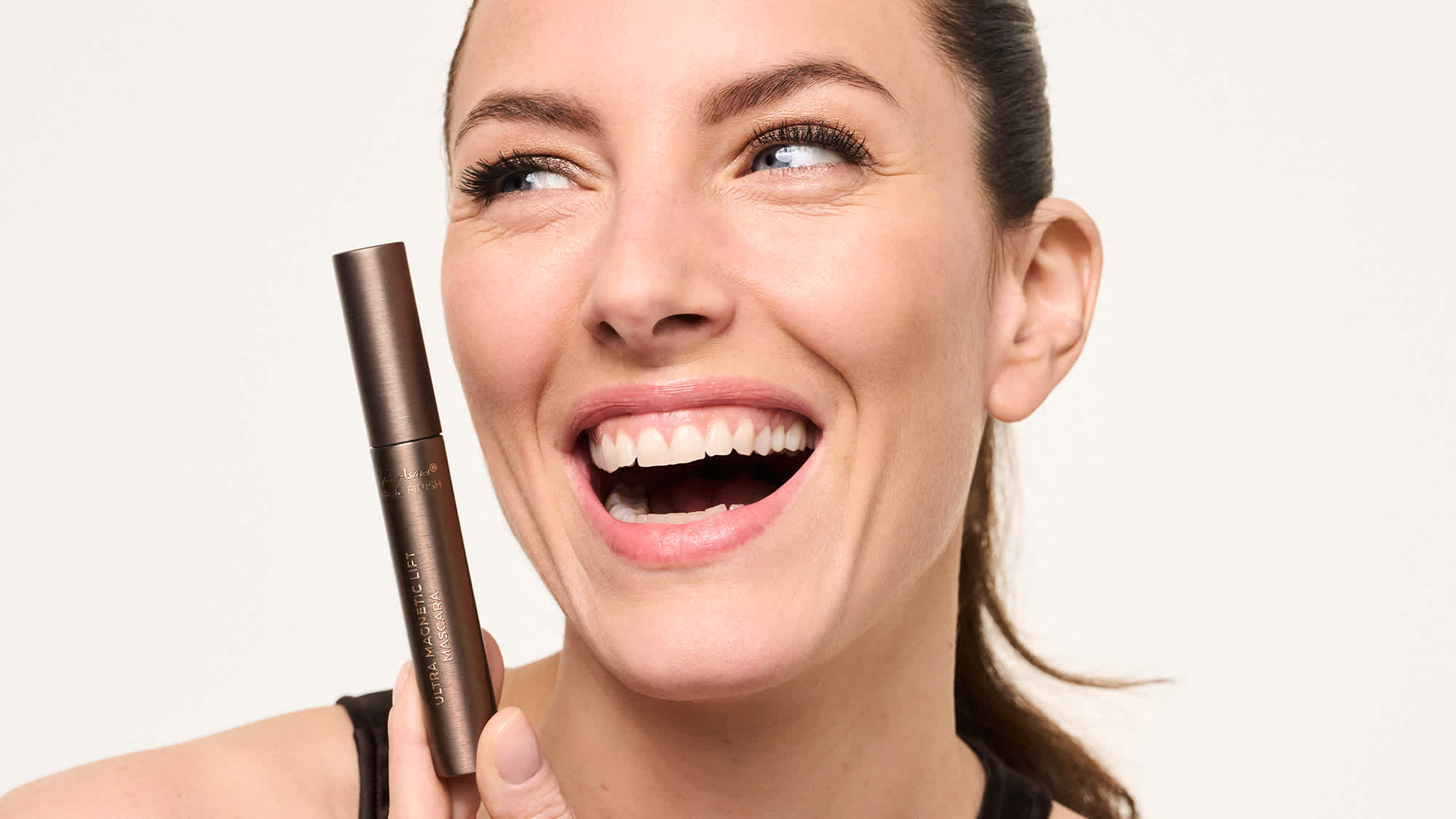 Lächelndes Model mit Ultra Magnetic Lift Mascara in der Hand