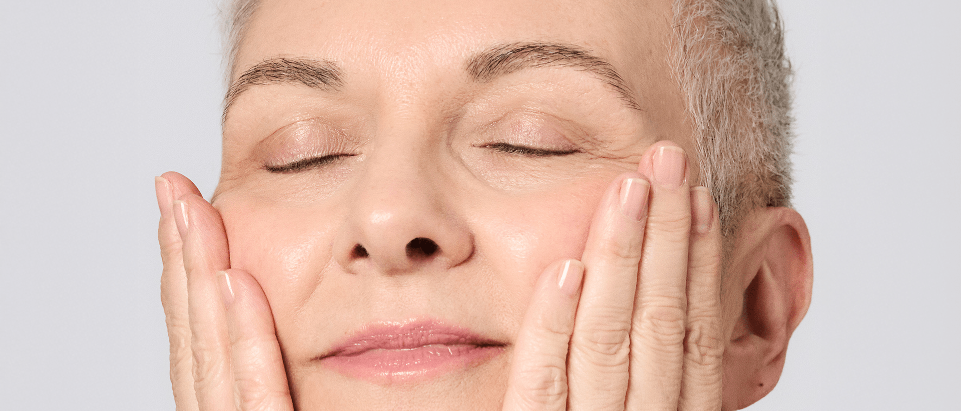 Femme aux yeux fermés touchant ses joues et appréciant la sensation sur la peau après l’application des soins VINOLIFT.