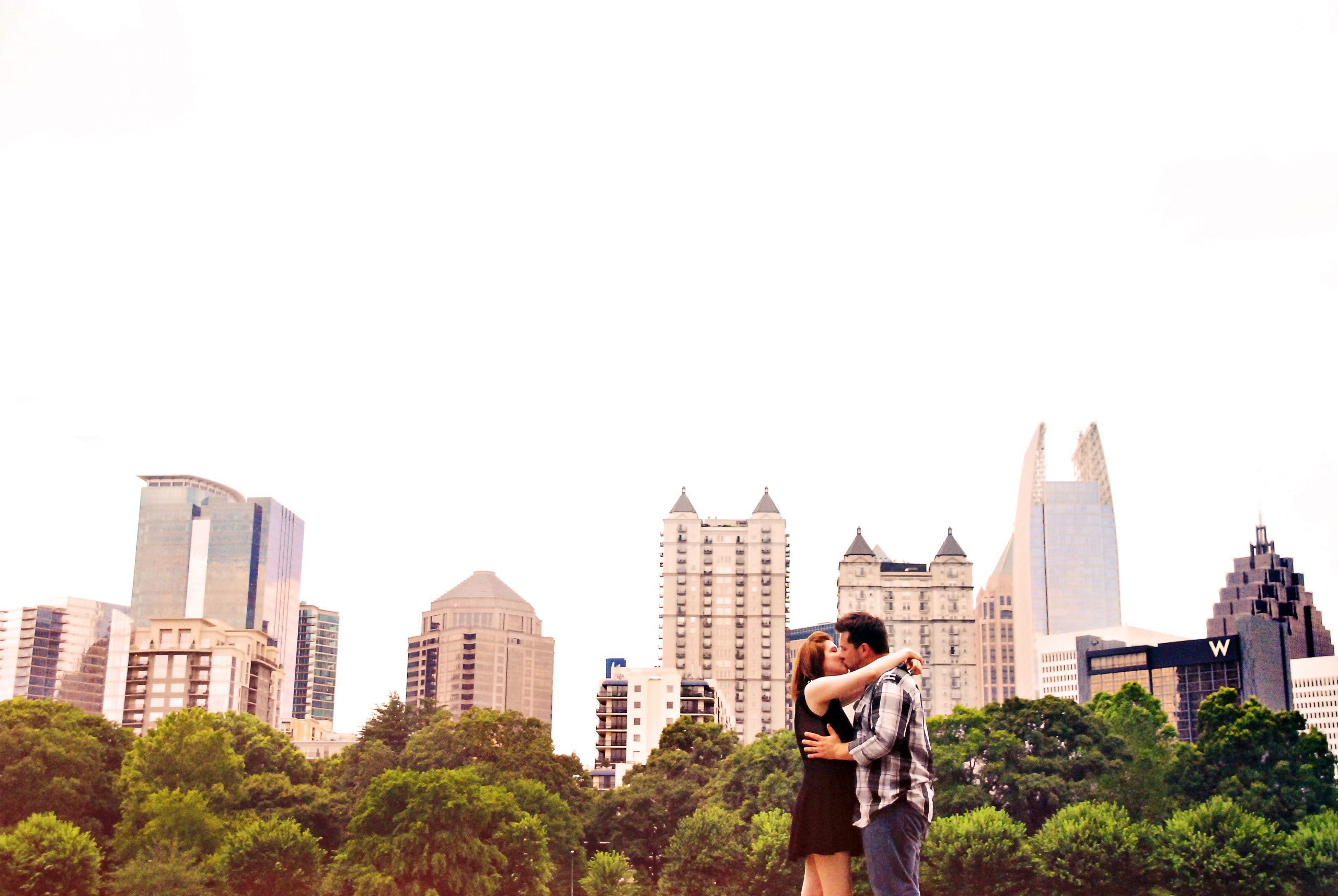 Couple kissing in Piedmont Park with the Atlanta skyline behind them.