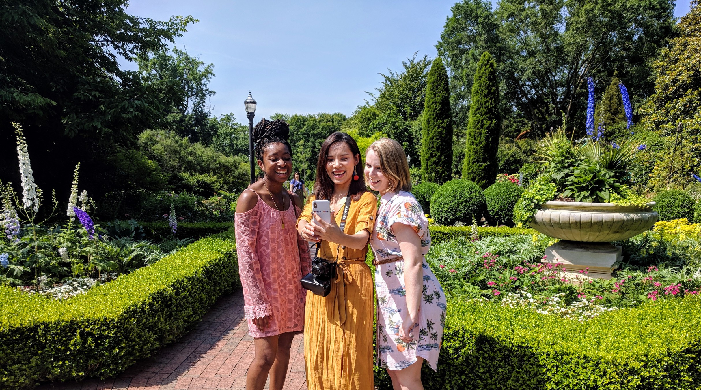 Three girlfriends smile and take a selfie among the garden at Atlanta Botanical Garden. 