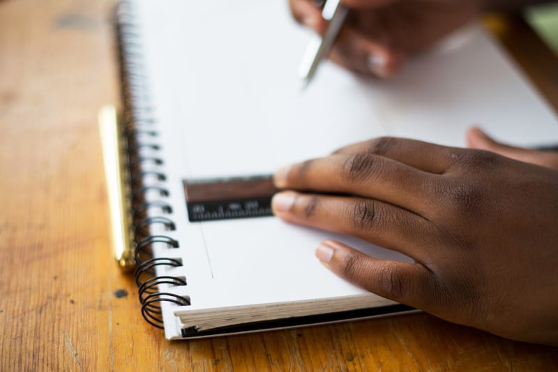 A teen's hands are shown drawing lines in a sketchbook with a pencil and ruler.