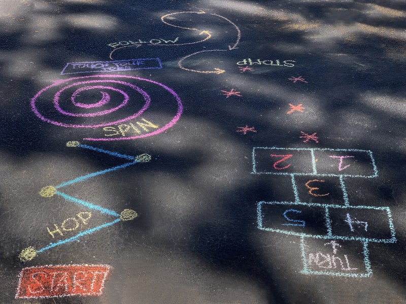 A sidewalk obstacle course drawn in chalk, that includes prompts like hop, spin, follow, stomp, and turn.