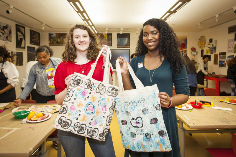 Two teen girls holding up tote bags they printed during Teen Night at the High Museum of Art Atlanta.