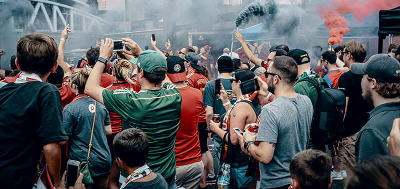 A large crowd of people, many wearing red, gather in a smoky outdoor area, holding up their phones in Atlanta, Georgia.