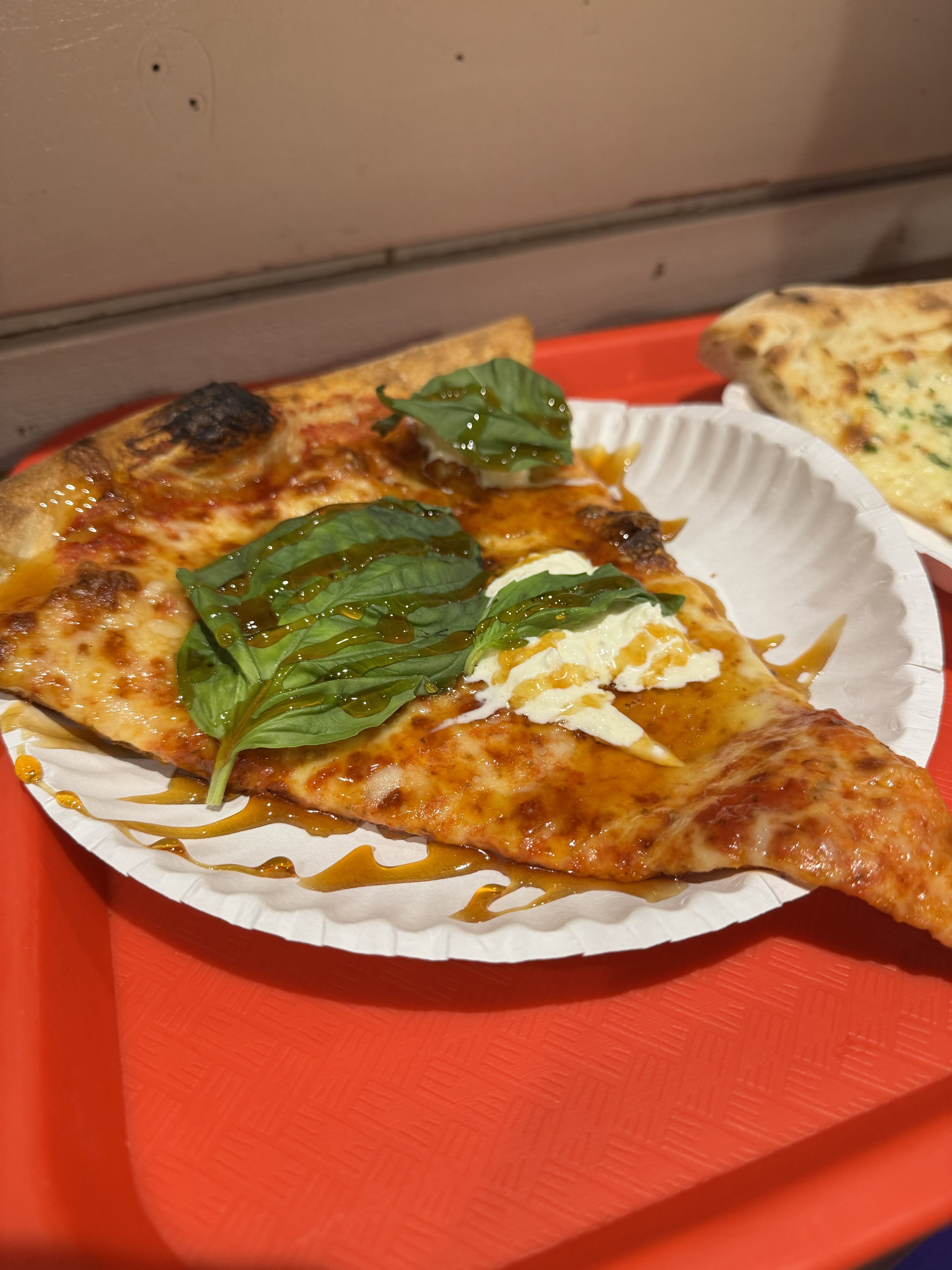 Tour Atlanta Beltline From Krog Street Market to Ponce City Market 4 A slice of pizza topped with fresh basil leaves and dollops of creamy cheese sits on a white paper plate, drizzled with a golden syrup, all resting on a vibrant red tray in Atlanta, Georgia.