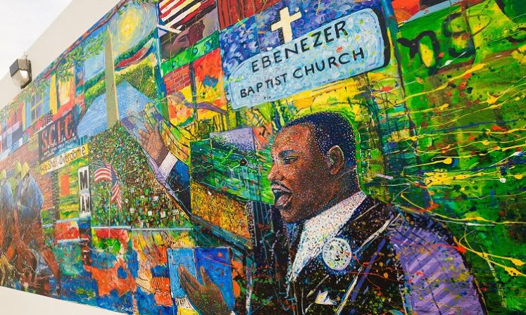 A vibrant mural depicting Martin Luther King Jr. speaking to a crowd with American flags and religious symbols in Atlanta, Georgia.