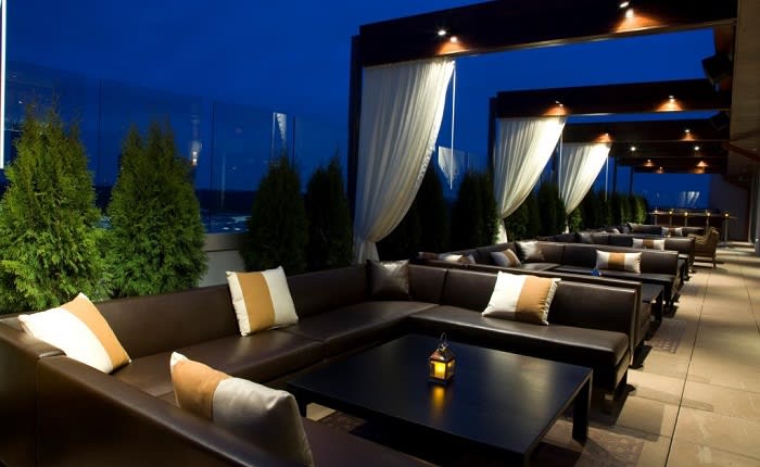 An outdoor rooftop lounge with leather sofas, curtains, and potted plants at dusk in Atlanta, Georgia.
