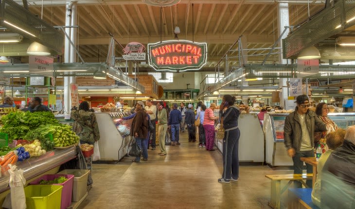 A bustling indoor farmers market filled with fresh produce, meats, and cheeses, with a prominent neon sign reading 'Municipal Market' overhead in Atlanta, Georgia.