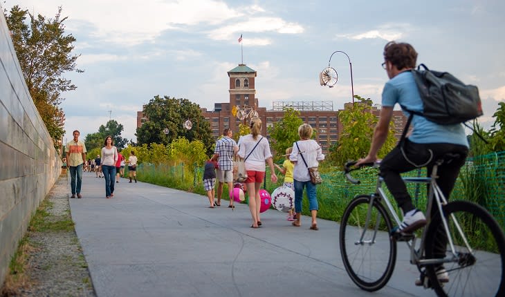 A group of people enjoys a sunny day on a paved path alongside a river in Atlanta, Georgia.