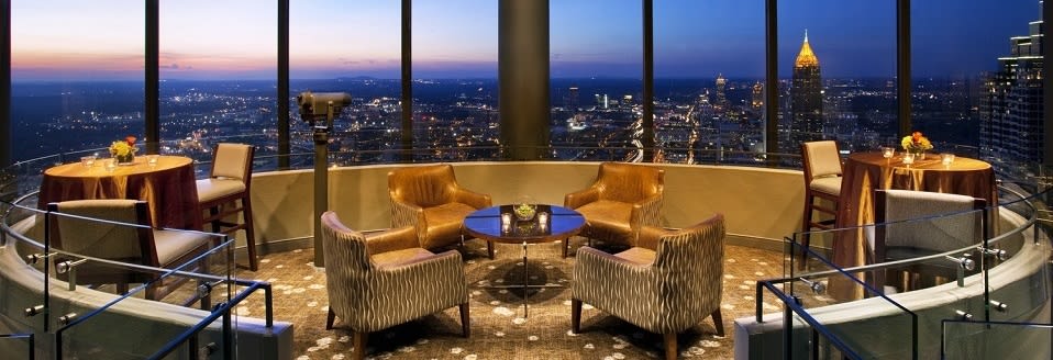 A rooftop lounge with leather chairs and tables overlooking a city skyline at dusk in Atlanta, Georgia.