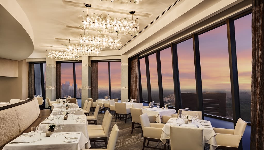 A modern restaurant with floor-to-ceiling windows overlooking a city skyline at sunset in Atlanta, Georgia.