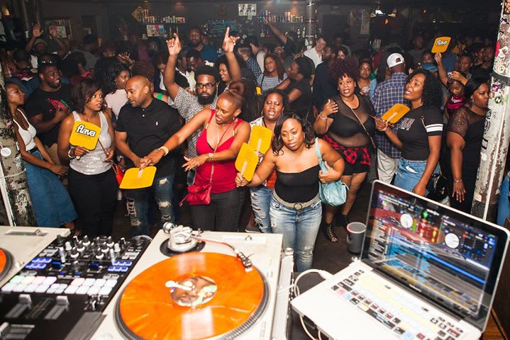 Crowded nightclub dance floor with people holding up yellow cards, DJ booth in foreground in Atlanta, Georgia.