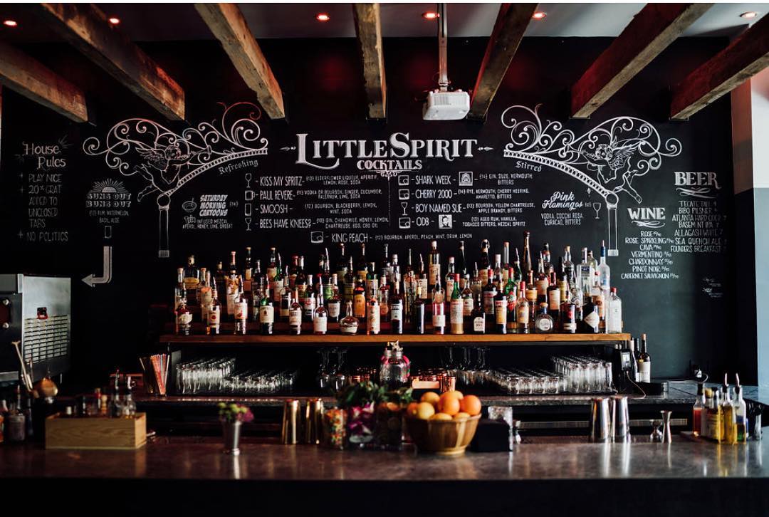 A rustic bar with exposed beams, chalkboard menus, and a wall of liquor bottles in Atlanta, Georgia.