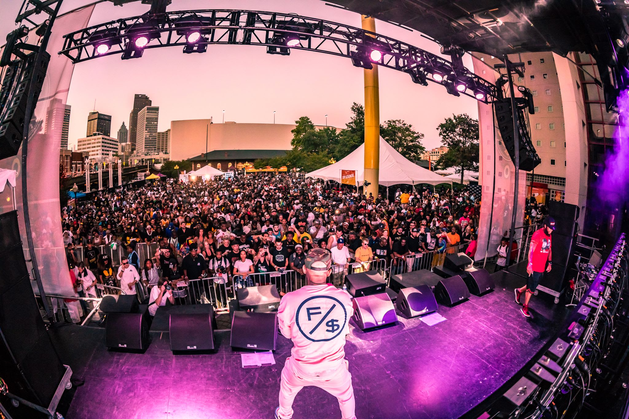 A rapper performs on a brightly lit stage in front of a massive crowd at an outdoor concert in Atlanta, Georgia.