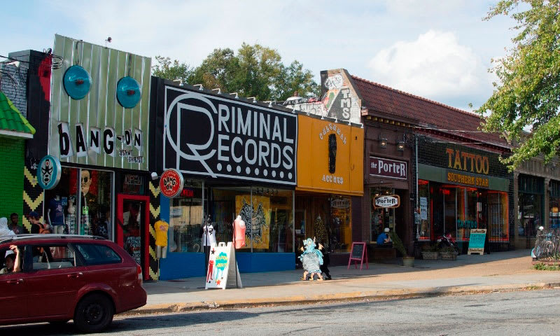 Colorful storefronts line a street, featuring a record store, tattoo parlor, and other eclectic shops in Atlanta, Georgia.