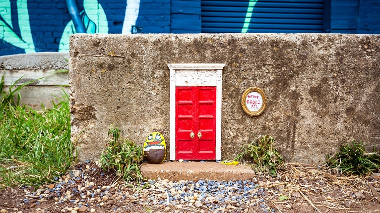 A whimsical fairy door with a red frame and white trim is set into a concrete wall in Atlanta, Georgia.