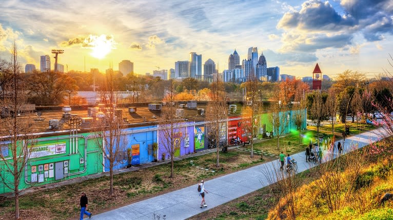 Sunlit city skyline with colorful murals and people walking on a path in Atlanta, Georgia.
