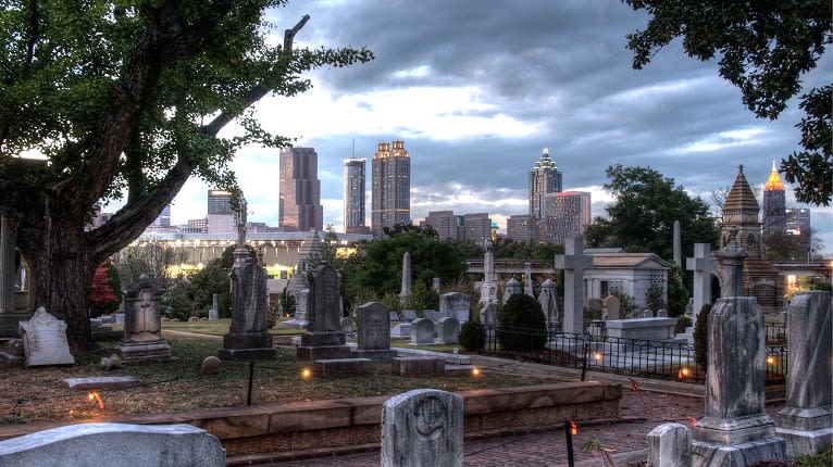 A serene cemetery with tall gravestones and lush trees overlooks a modern city skyline in Atlanta, Georgia.