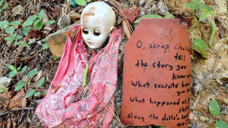 A weathered doll with a cracked head lies on the ground next to a broken clay pot with handwritten text in Atlanta, Georgia.