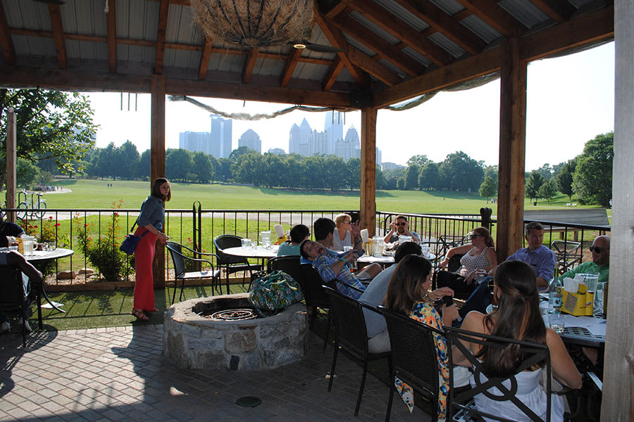 Outdoor restaurant patio with people dining, stone fireplace, and city skyline view in Atlanta, Georgia.