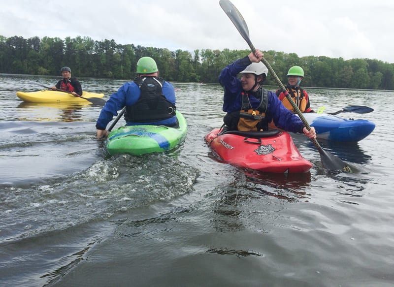 A group of kayakers paddle on a calm lake surrounded by trees in Atlanta, Georgia.