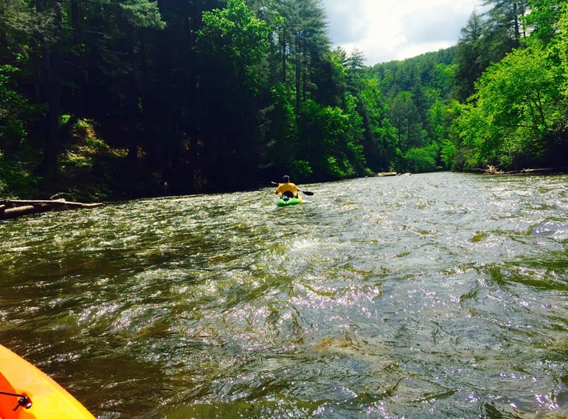 A kayaker paddles down a fast-flowing river surrounded by lush green forest in Atlanta, Georgia.