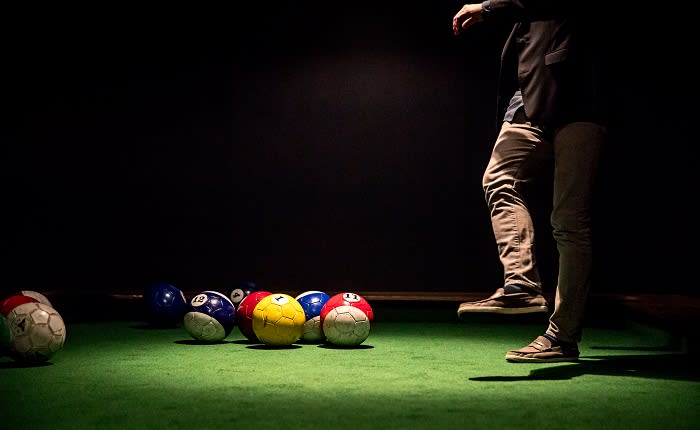 A person stands near colorful balls on a green surface in a dimly lit room in Atlanta, Georgia.