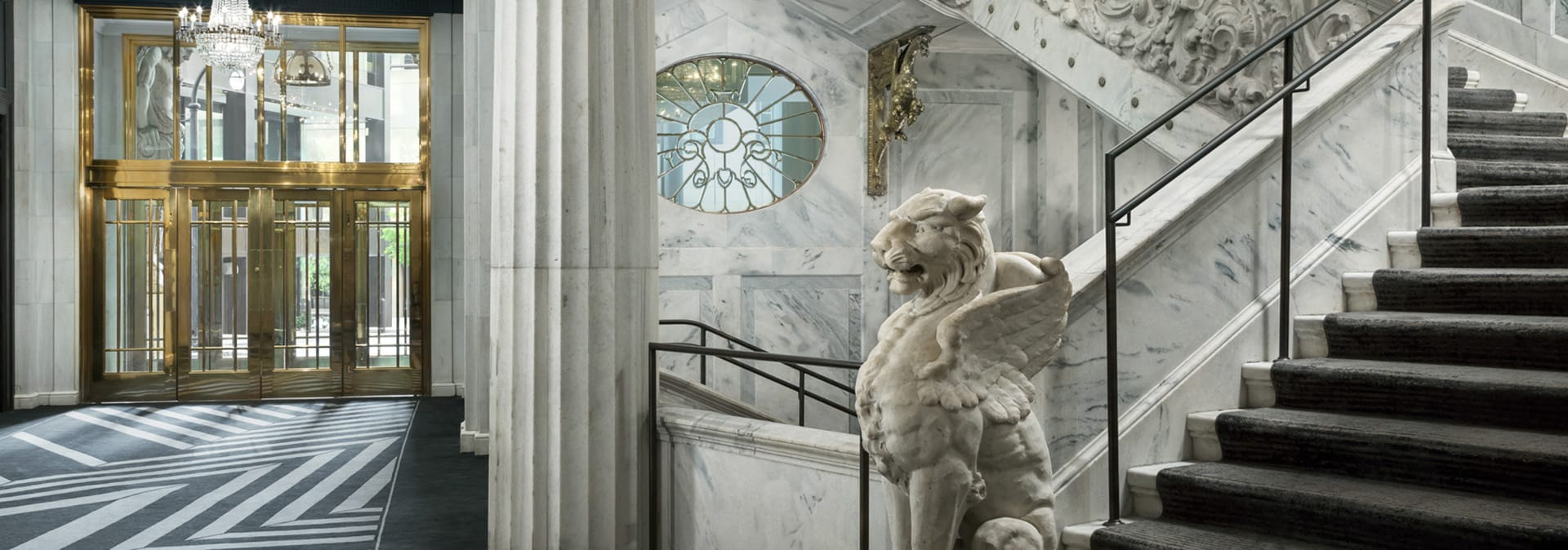A grand marble staircase with a lion statue and ornate railings leads up to a chandelier-lit entrance in Atlanta, Georgia.