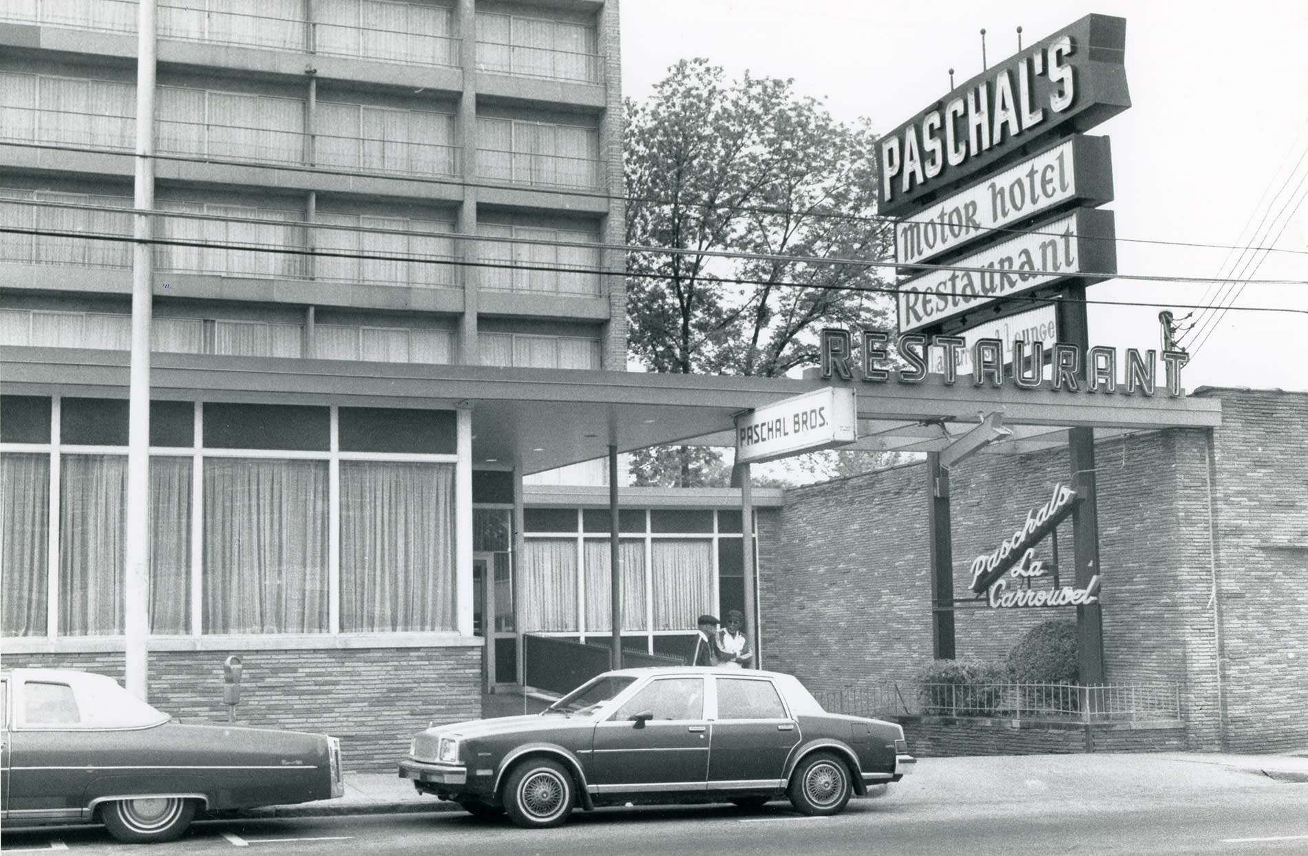 A black and white photo of a vintage motel with a prominent neon sign advertising a restaurant and bar in Atlanta, Georgia.