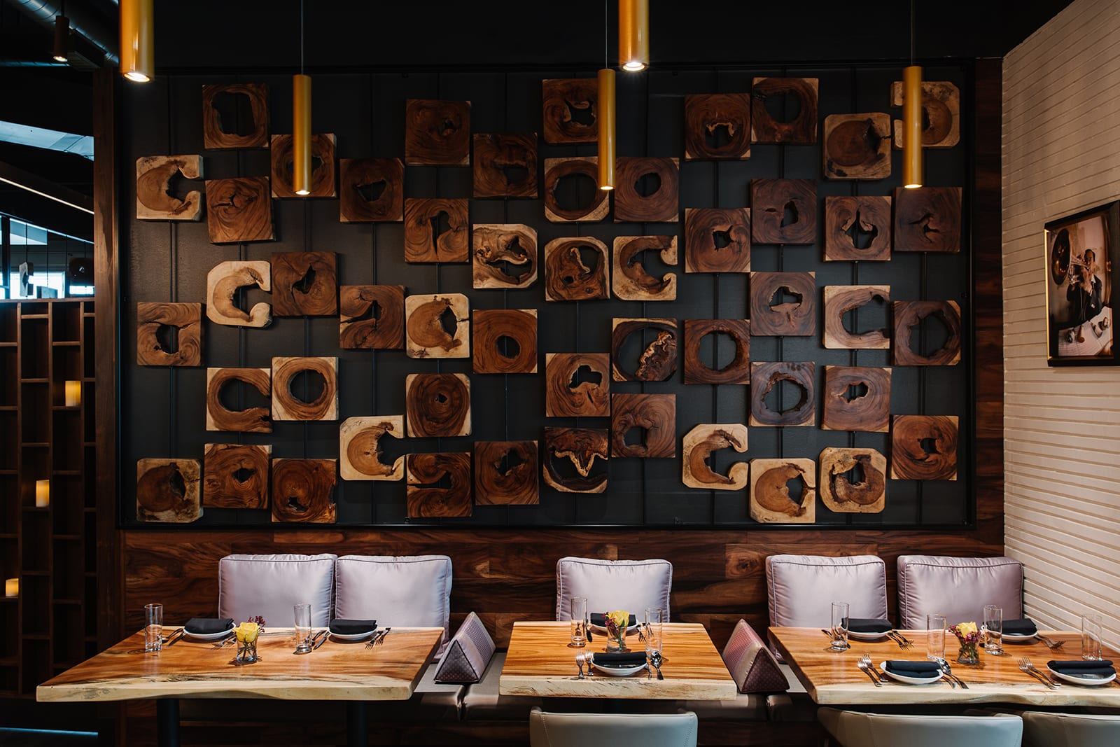 A modern restaurant interior with wooden tables, plush seating, and a striking wall of circular wood art in Atlanta, Georgia.