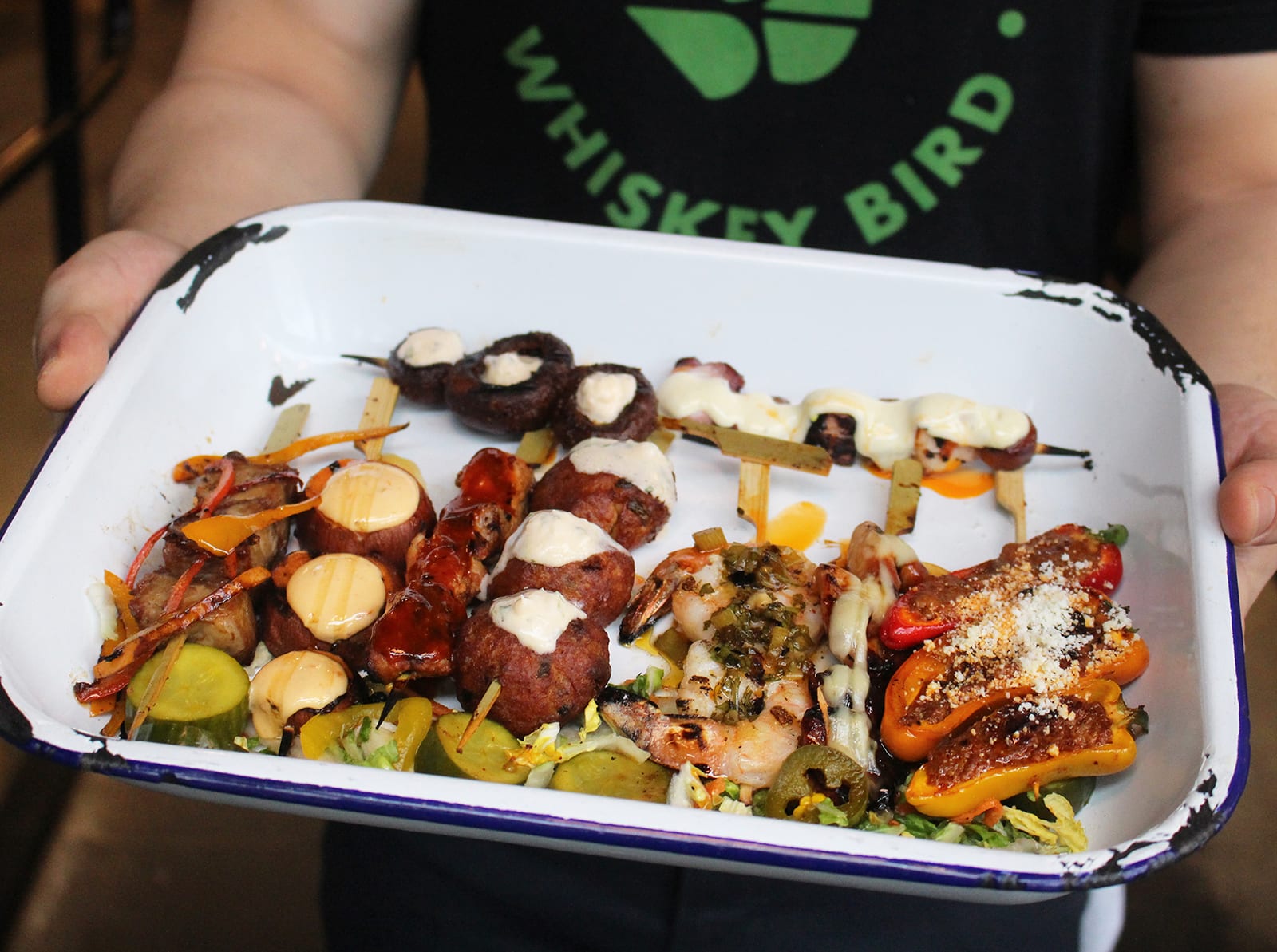 A person holds a tray of colorful skewered appetizers, including mushrooms, peppers, and shrimp in Atlanta, Georgia.