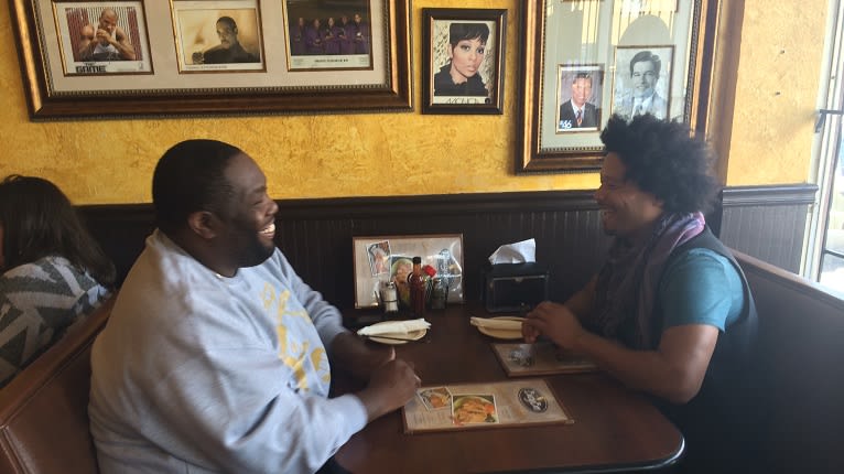 Two men share a laugh over a meal in a cozy restaurant booth in Atlanta, Georgia.