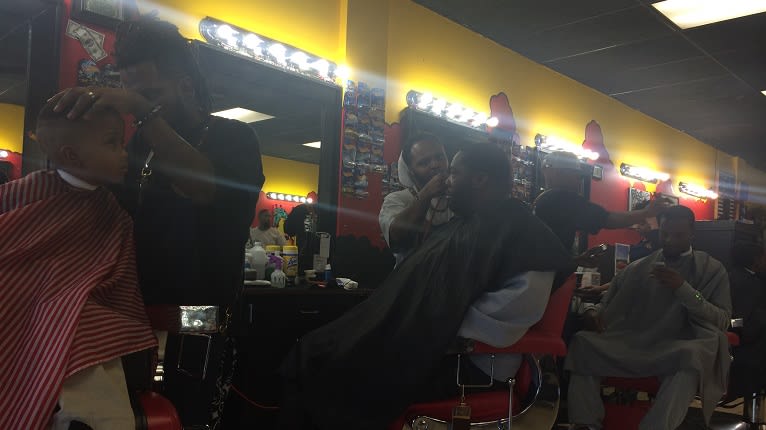 A busy barbershop with multiple barbers cutting hair, including a child getting a haircut in Atlanta, Georgia.